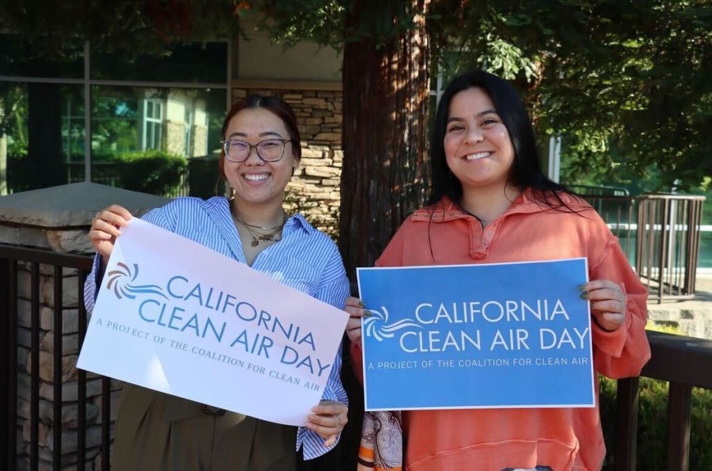 Two smiling people holding up Clean Air Day signs